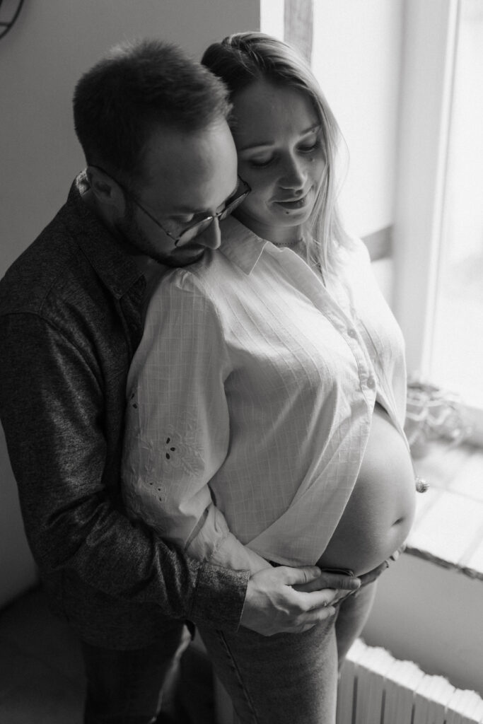 Papa embrassant l'épaule de la maman, tous deux tenant le ventre de grossesse, photo artistique N&B.