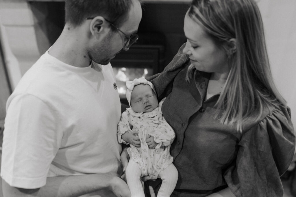 Gros plan noir et blanc des parents devant une cheminée, bébé au centre.
