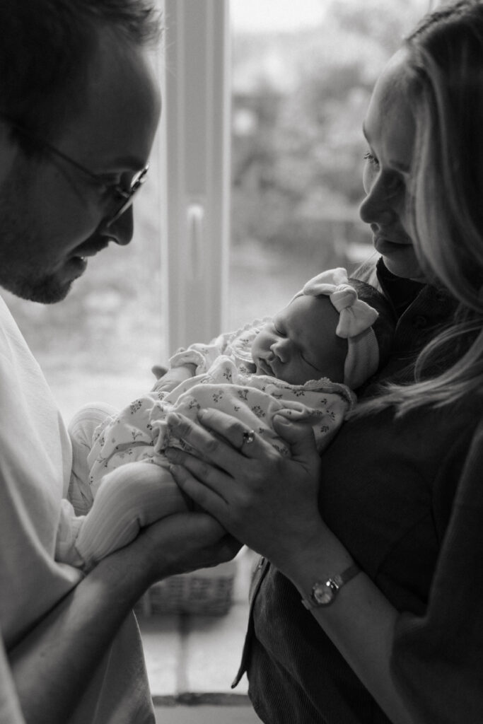 Parents en contre-jour devant une fenêtre, regardant leur bébé tendrement à Reims.