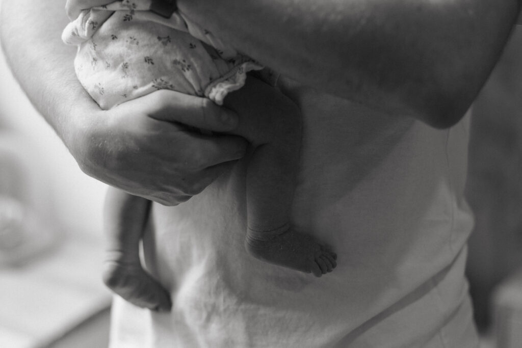 Pieds nus de bébé dans le vide tenus par papa, photo noir et blanc à Reims.