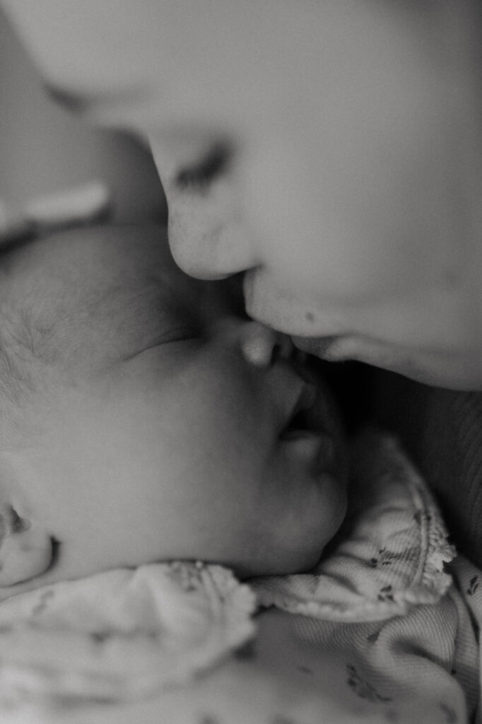 Portrait en noir et blanc : maman embrassant tendrement le nez de son bébé. Séance photo naissance à Reims.