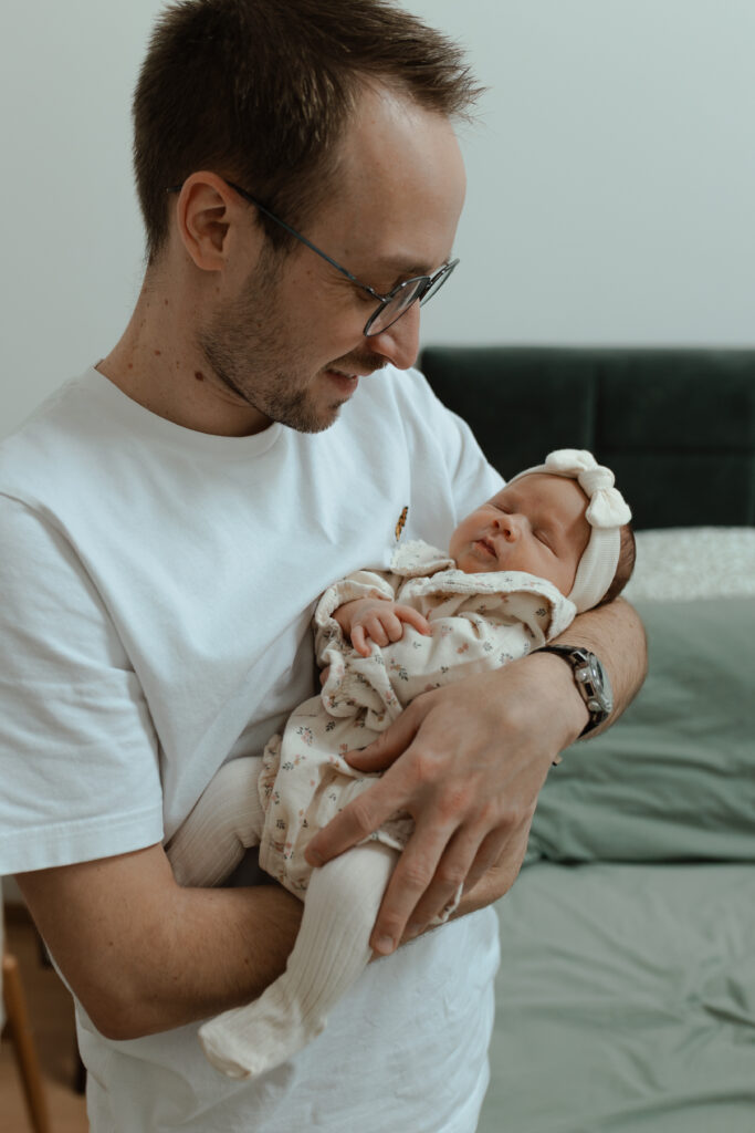 Papa souriant en regardant son bébé endormi dans ses bras à Reims.