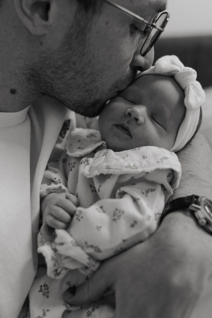 Gros plan en noir et blanc d'un papa embrassant la joue de son bébé.