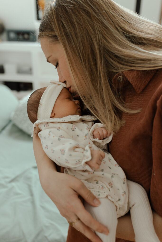 Gros plan : maman embrassant le front de son bébé endormi.