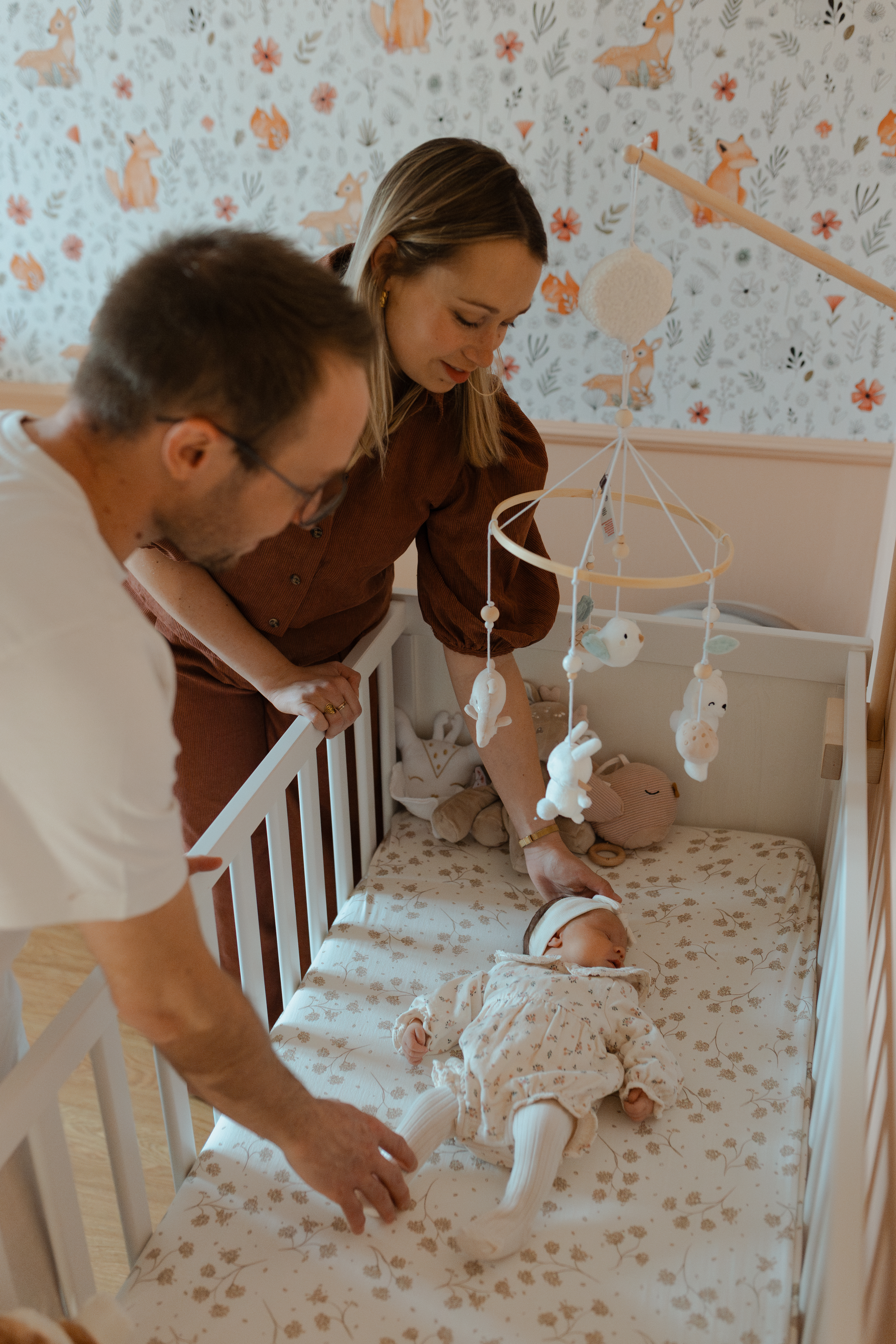 Parents tenant la main et le pied de leur bébé allongé dans son lit.