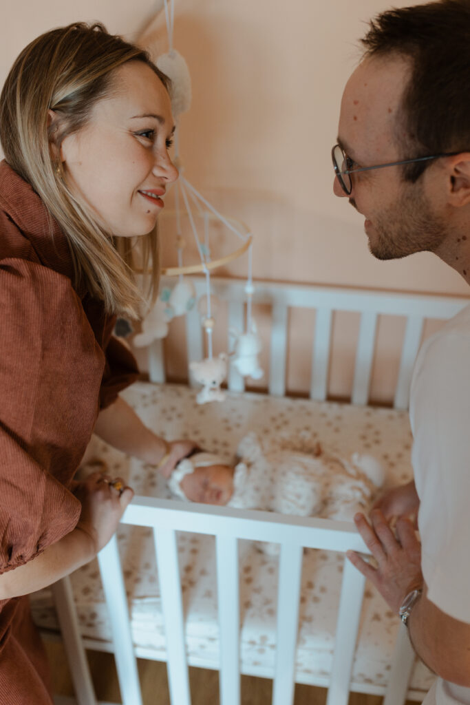 Parents nets se souriant avec bébé flou dans son lit en arrière-plan.