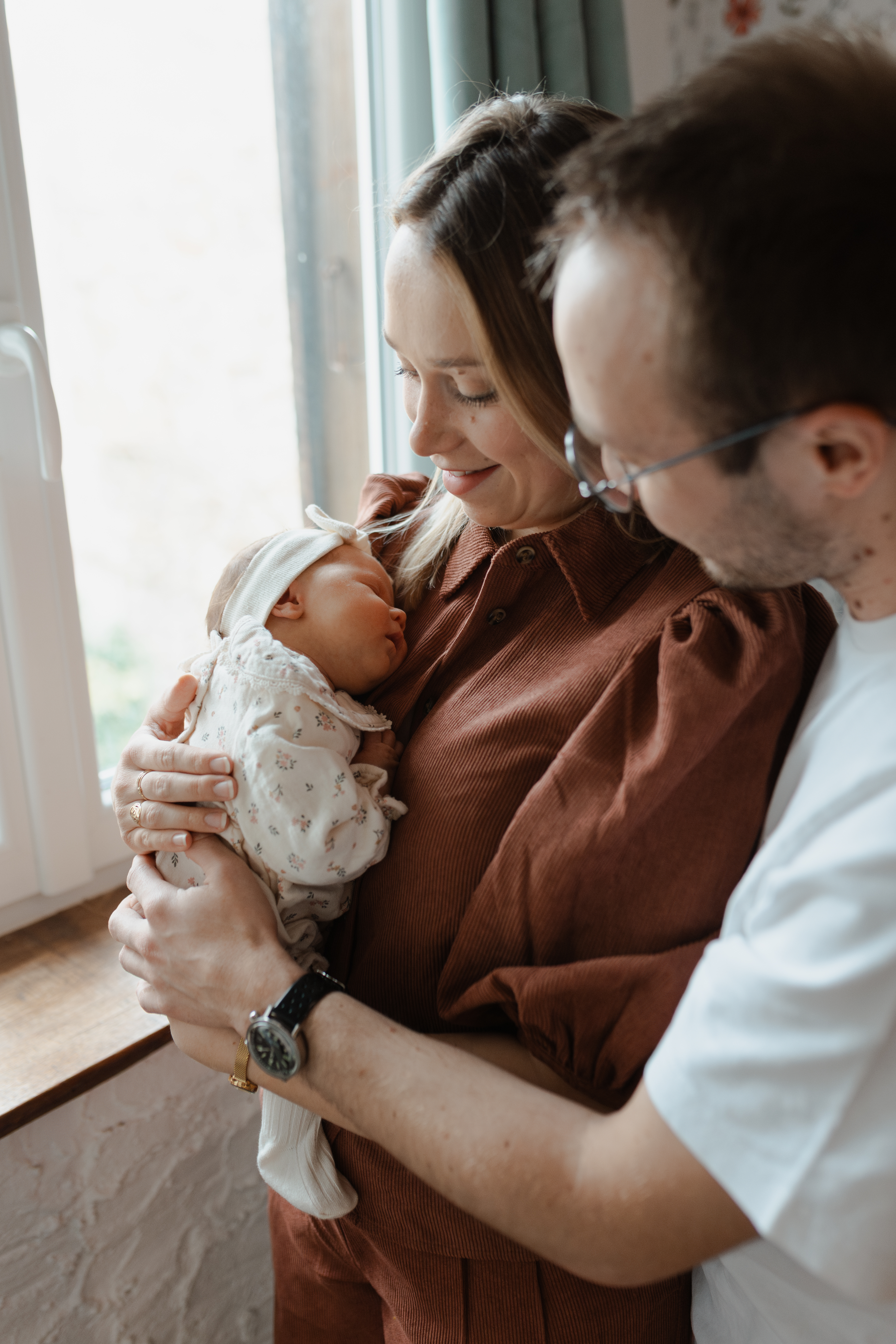 Parents tenant leur nouveau-né dans les bras dans une chambre baignée de lumière naturelle à Reims.
