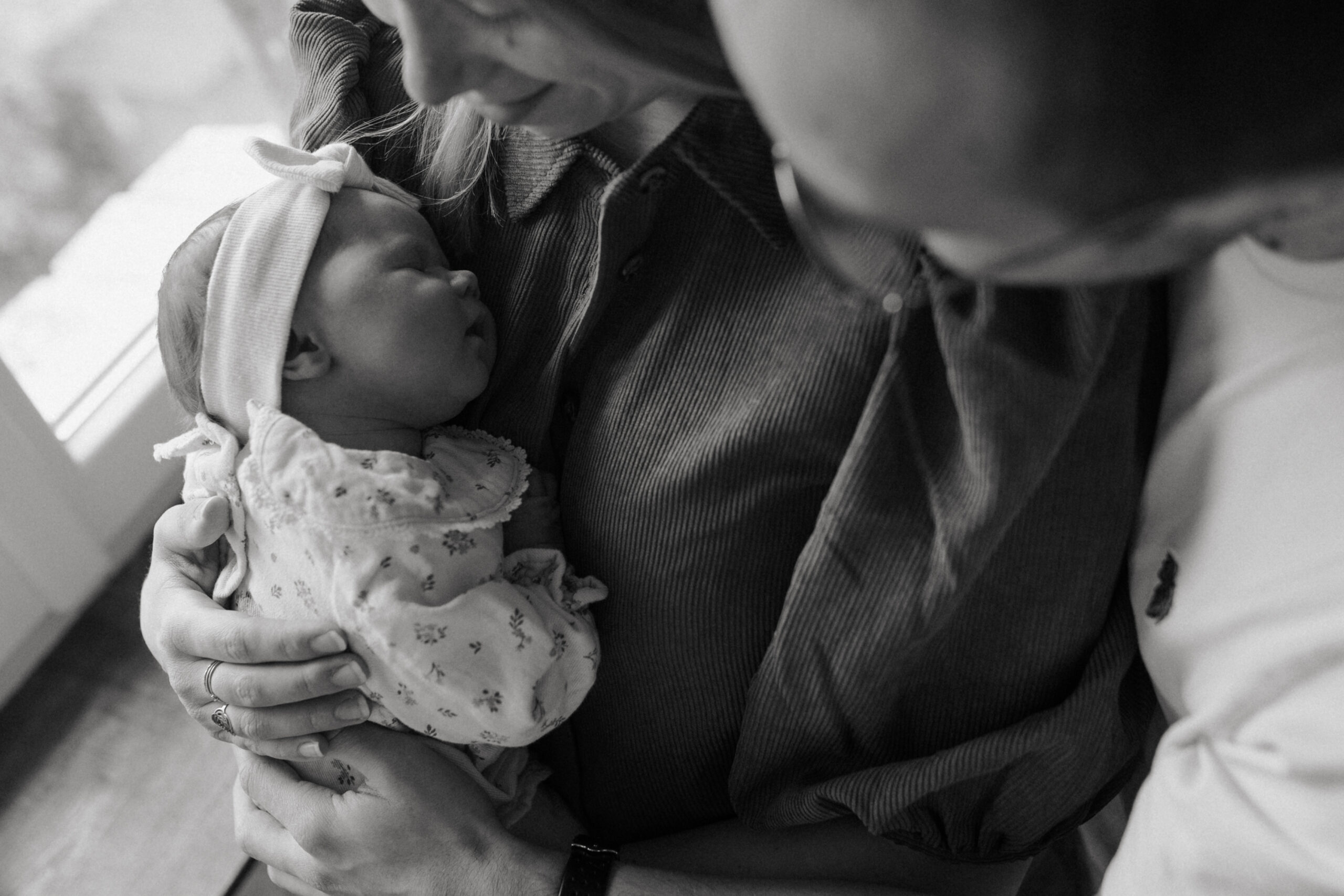 Gros plan noir et blanc d'un bébé assoupi contre sa maman, tenue par ses parents à Reims.