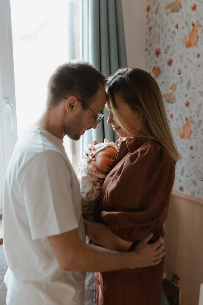 Parents face à face contemplant leur nouveau-né assoupi entre eux, front contre front à Reims.