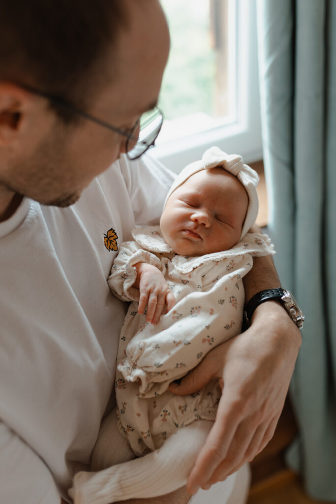 Papa regardant avec tendresse son nouveau-né endormi dans ses bras à Reims.