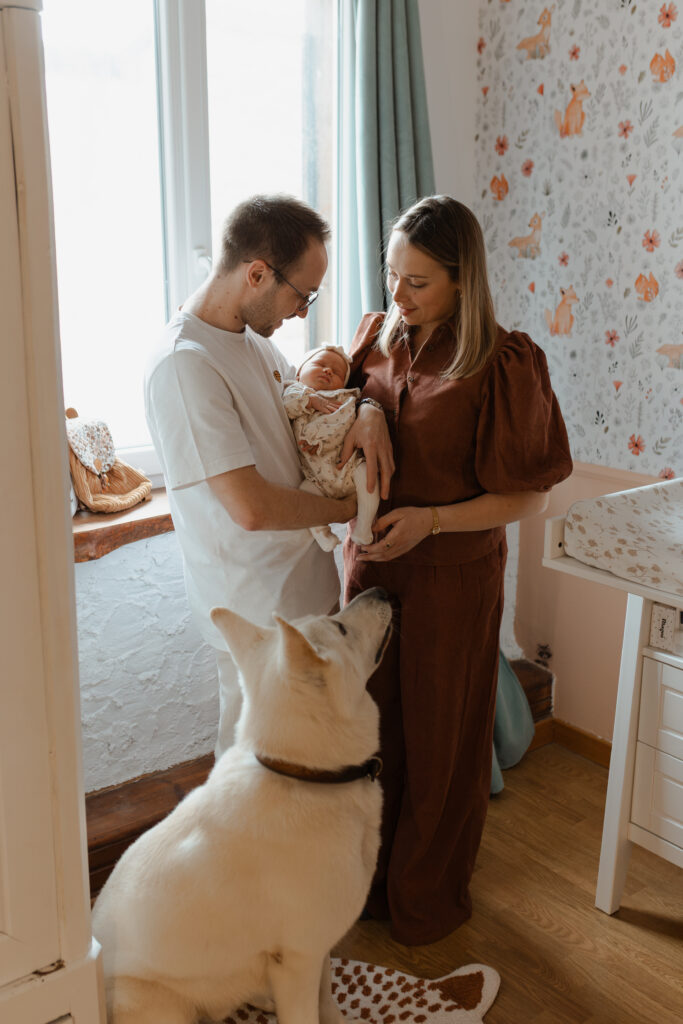 Parents et leur chien dans la chambre de bébé à Reims, tenant leur nouveau-né entre eux.