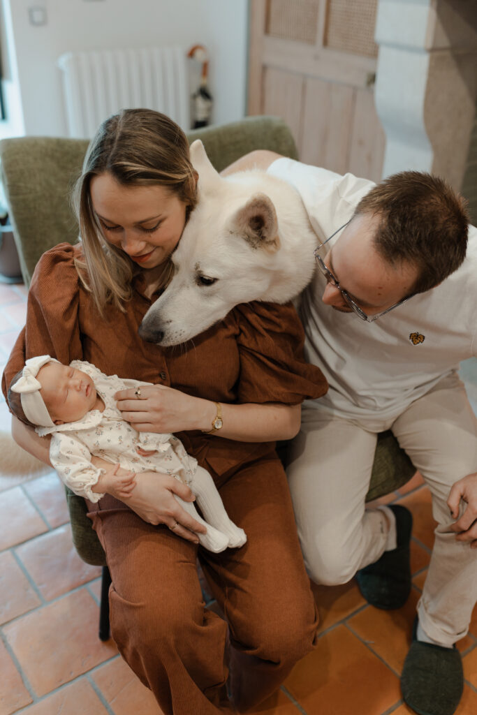 Couple assis dans un fauteuil avec leur bébé et leur chien les regardant tendrement à Reims.