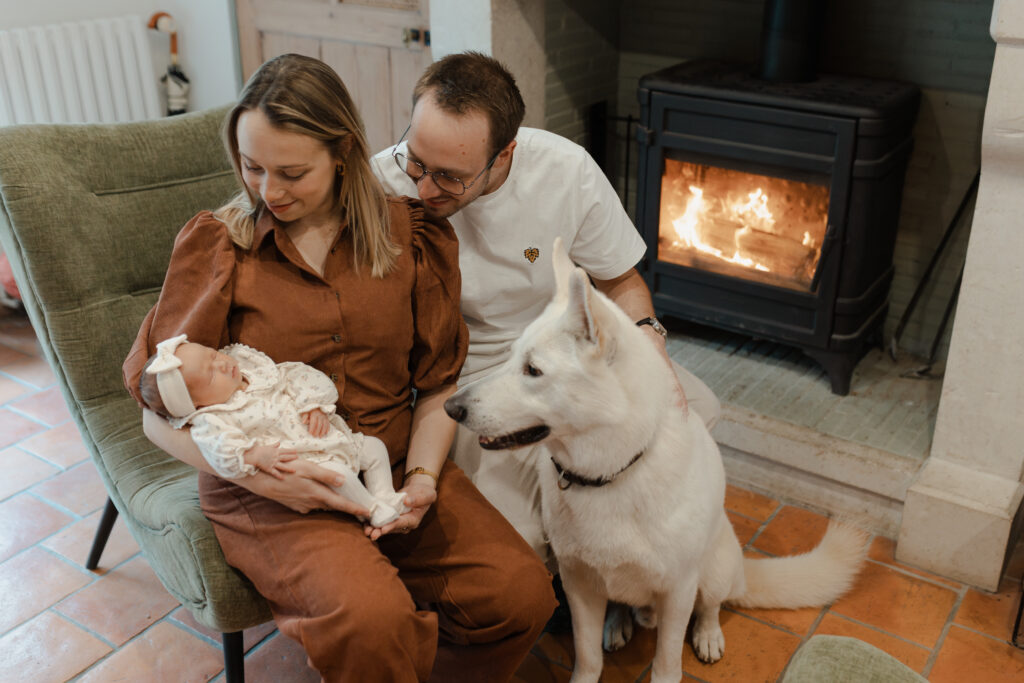 Famille avec leur chien devant une cheminée allumée lors d'une séance naissance à Reims.